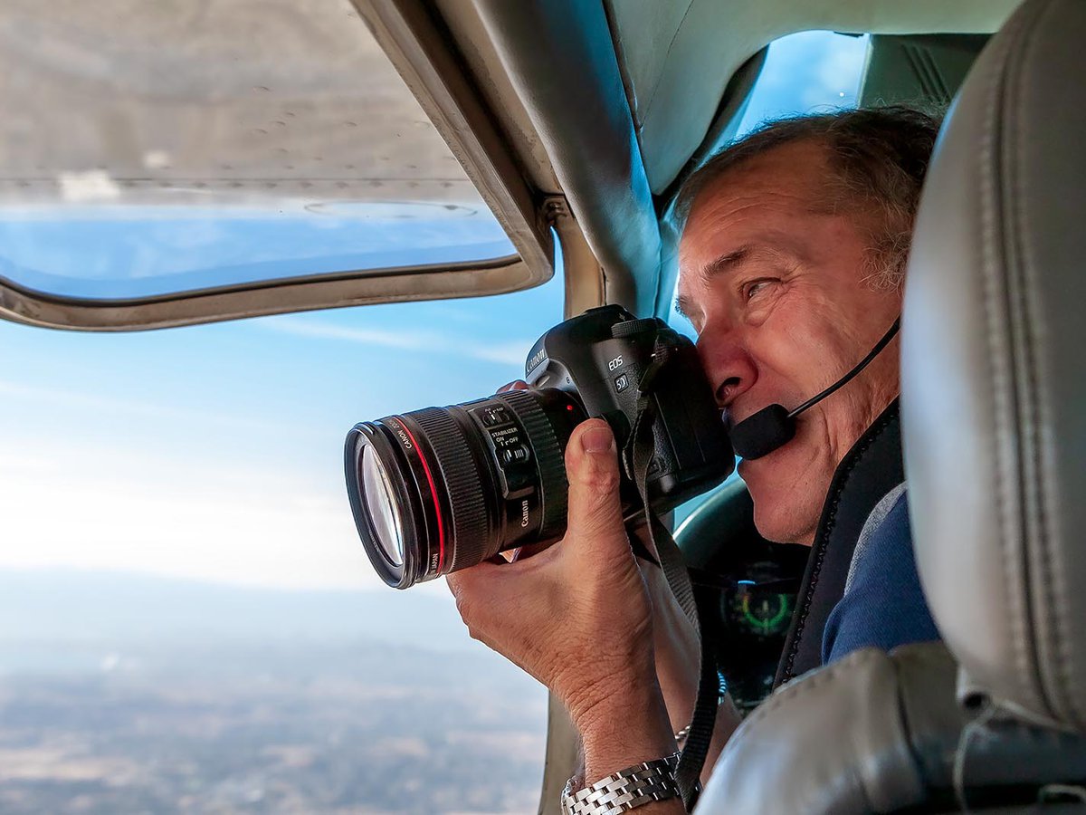 Press photo of Mark Holtzman taking aerial photographs through the window of his Cessna airplane
