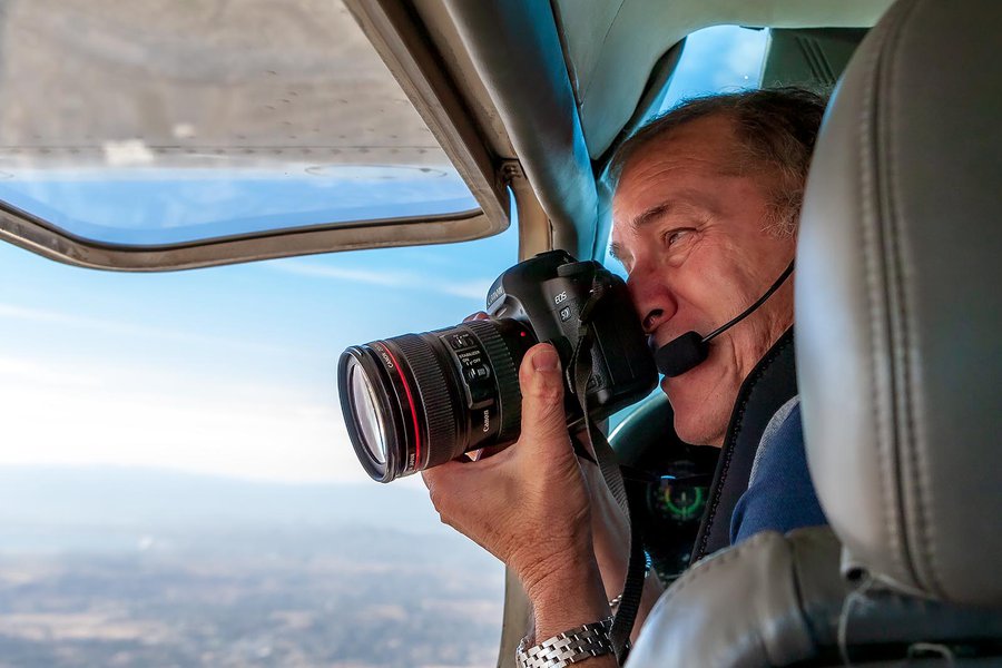 Press photo of Mark Holtzman taking aerial photographs through the window of his Cessna airplane